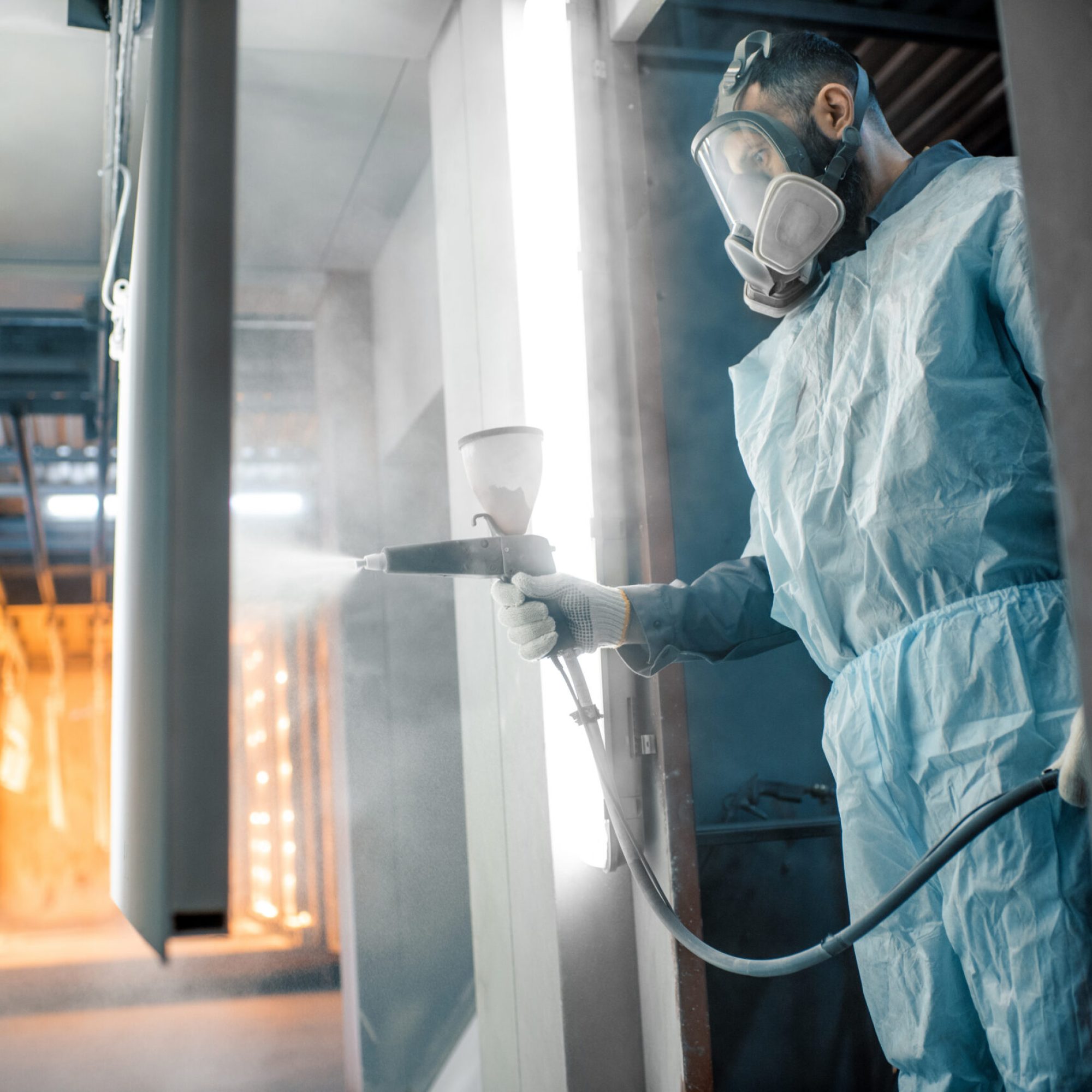 Painter in protective wear paints metal products with powder paint. Powder coating process at the manufacturing. High quality photo